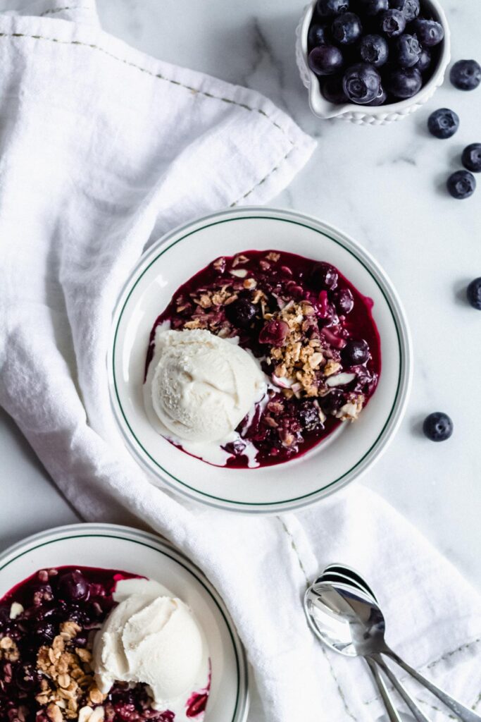 A bowl of blueberry crisp with ice cream.